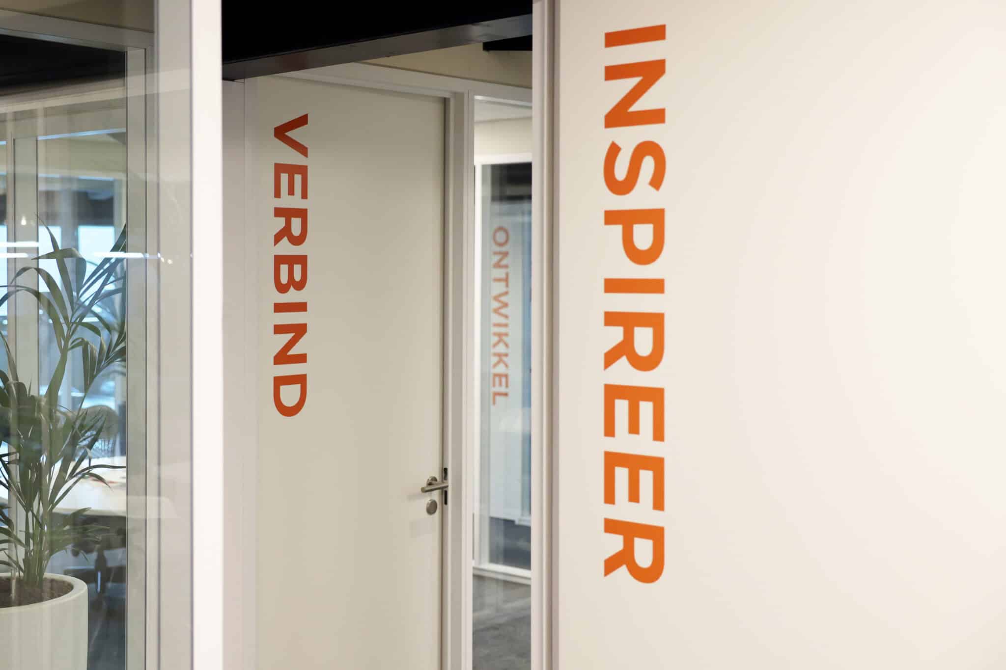 Deuren van een vergaderruimte met de woorden 'Inspireer', 'Verbind' en 'Ontwikkel' geschreven