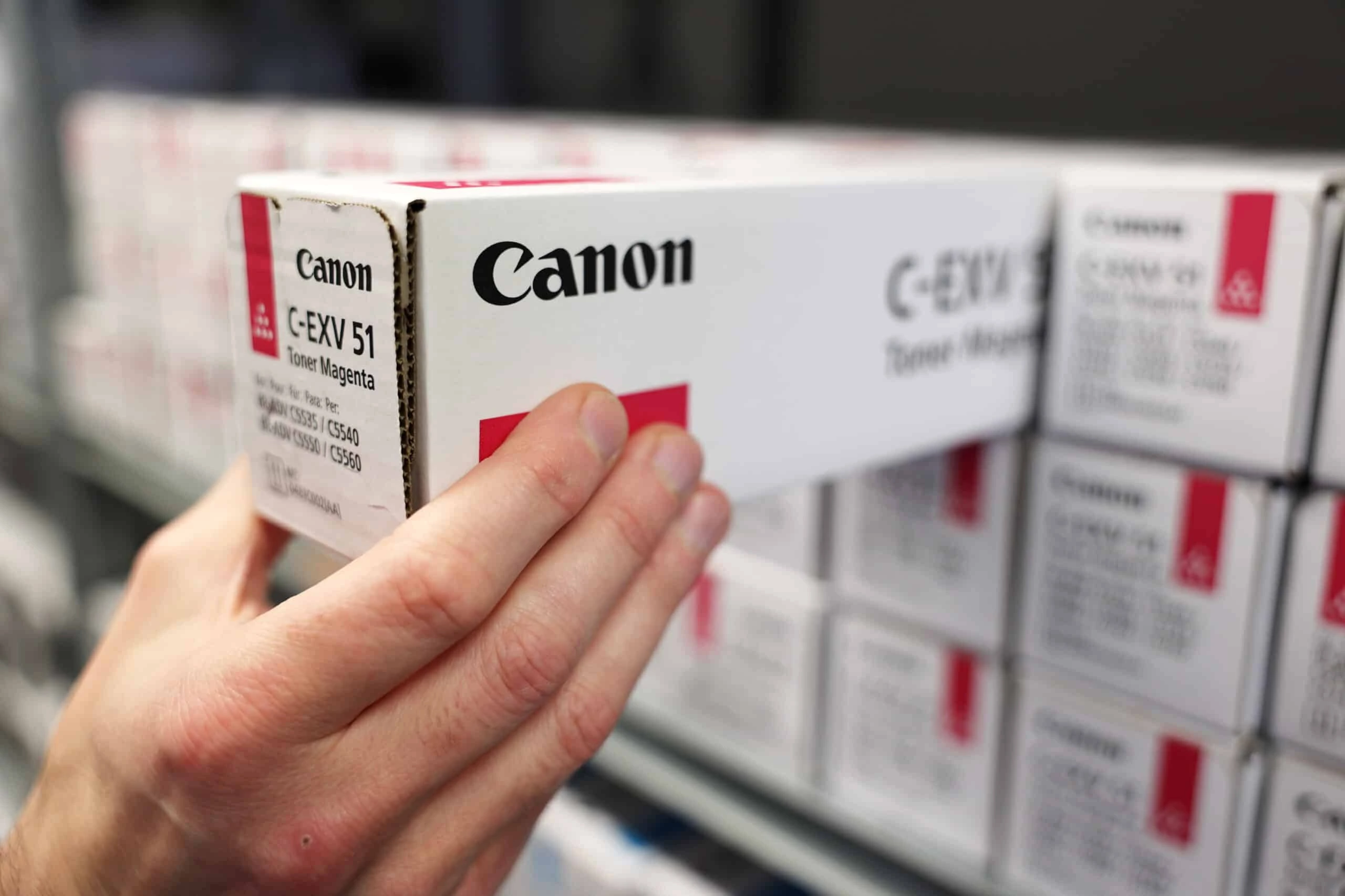 Een hand pakt een doos met Canon C-EXV 51 Toner Magenta van een plank vol met soortgelijke dozen – een voorbeeld van onze printoplossingen in de praktijk.